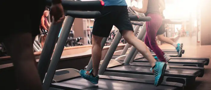 a row of treadmills with the lower half of people running on them