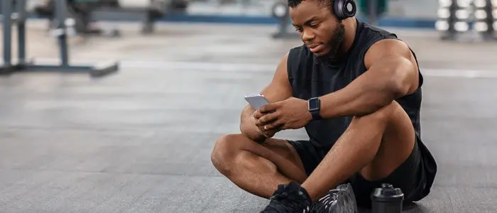Man sat on the floor of a gym on his phone