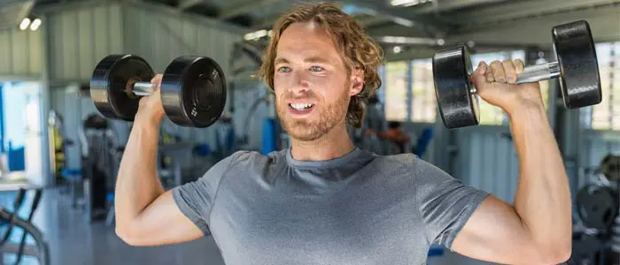 Man shoulder pressing dumbbells in a gym