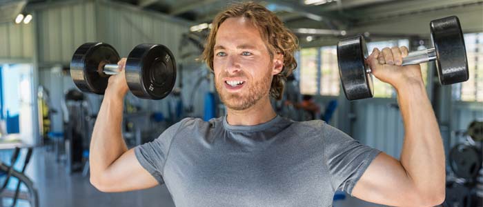 Man shoulder pressing dumbbells in a gym
